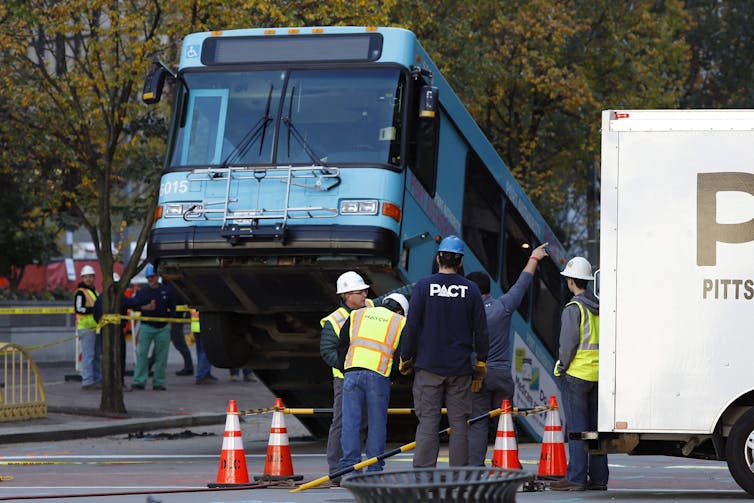 The front of a blue public transit bus pokes out of a sinkhole.