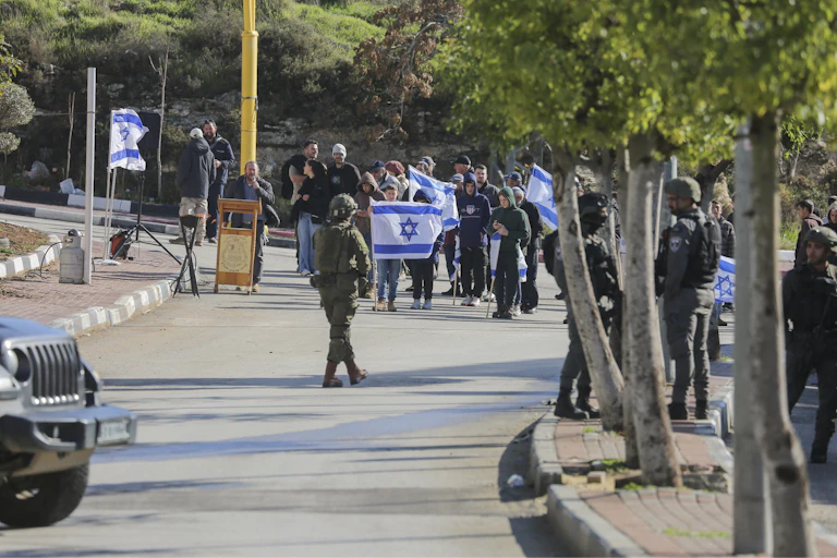 A groups of protestors with a large white and blue flag walk towards a man in uniform.