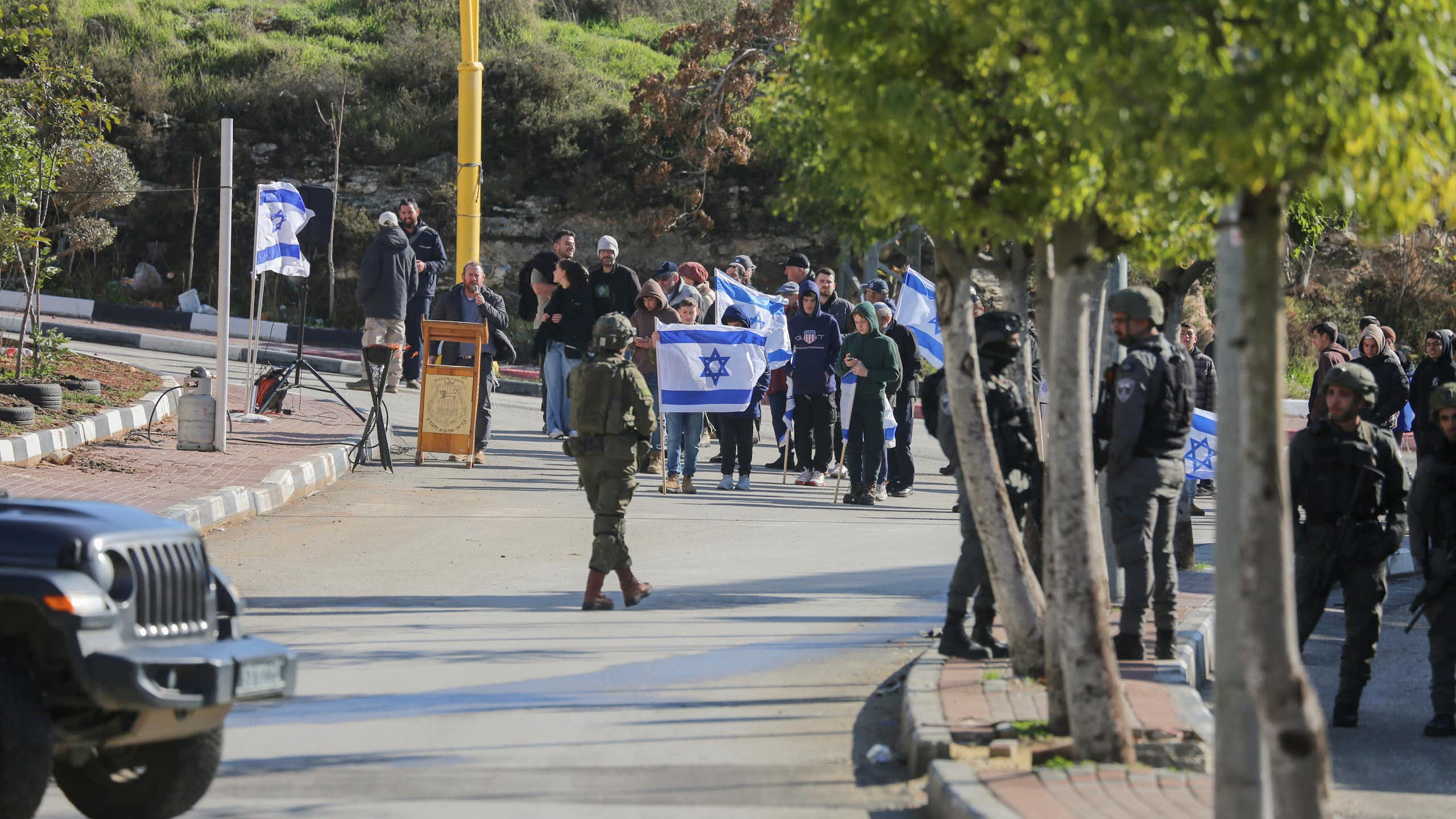 A groups of protestors with a large white and blue flag walk towards a man in uniform.