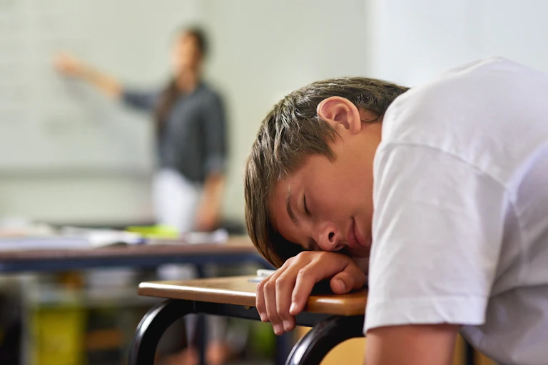 Um adolescente dormindo sobre a mesa da sala de aula.