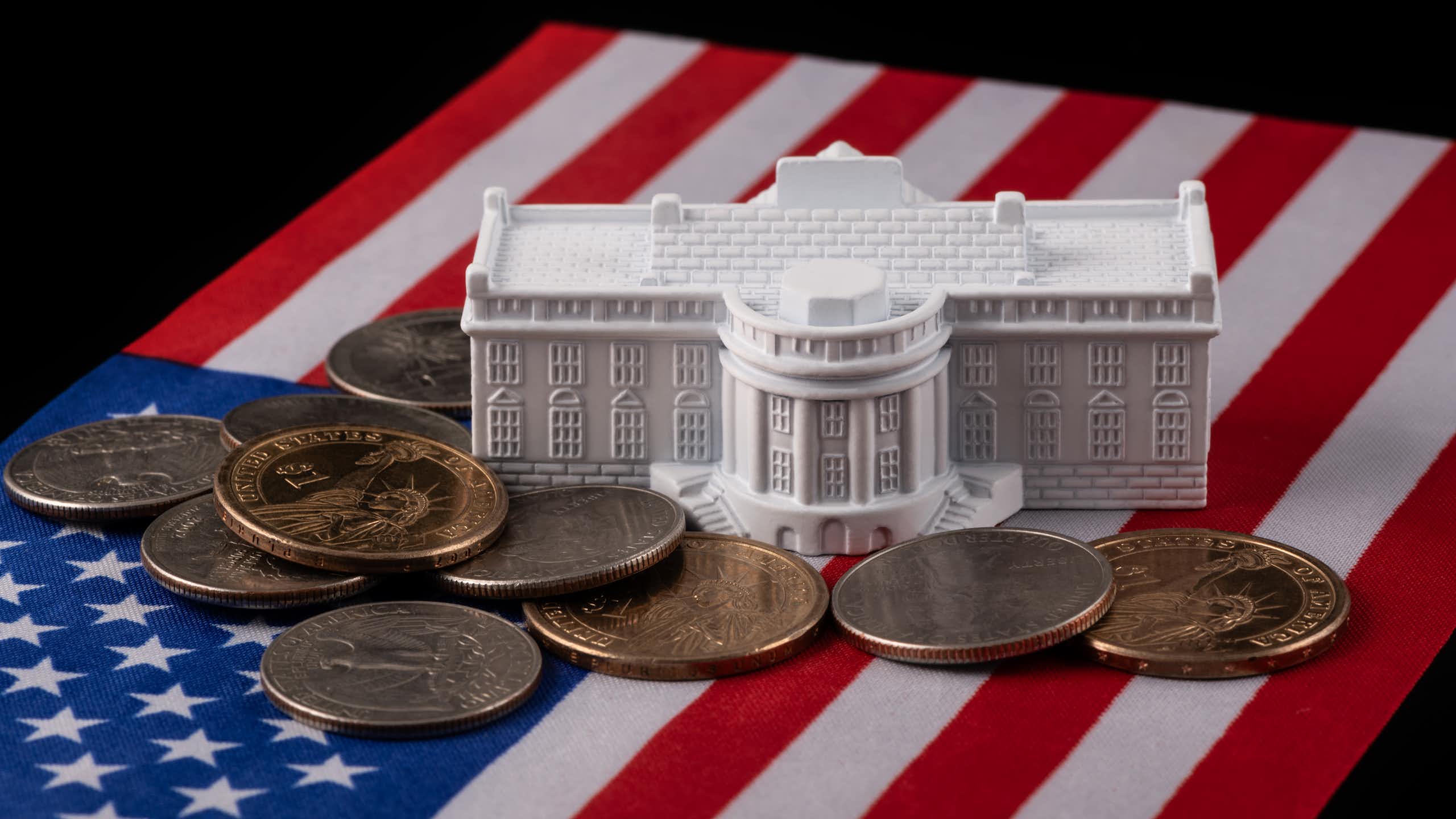 An American flag, with US coins and a model of the White House sitting on top of it.
