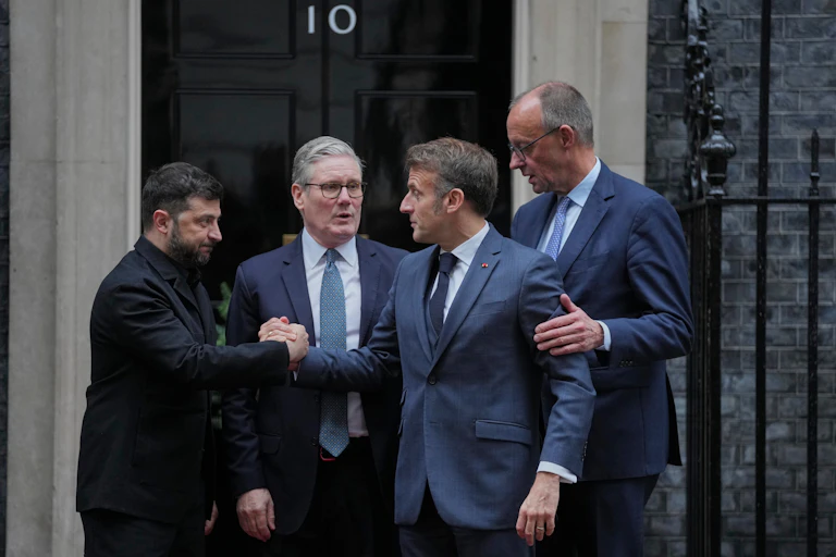 Four men in blue and black suits shake hands as they cluster outside a door with the number 10 on it.