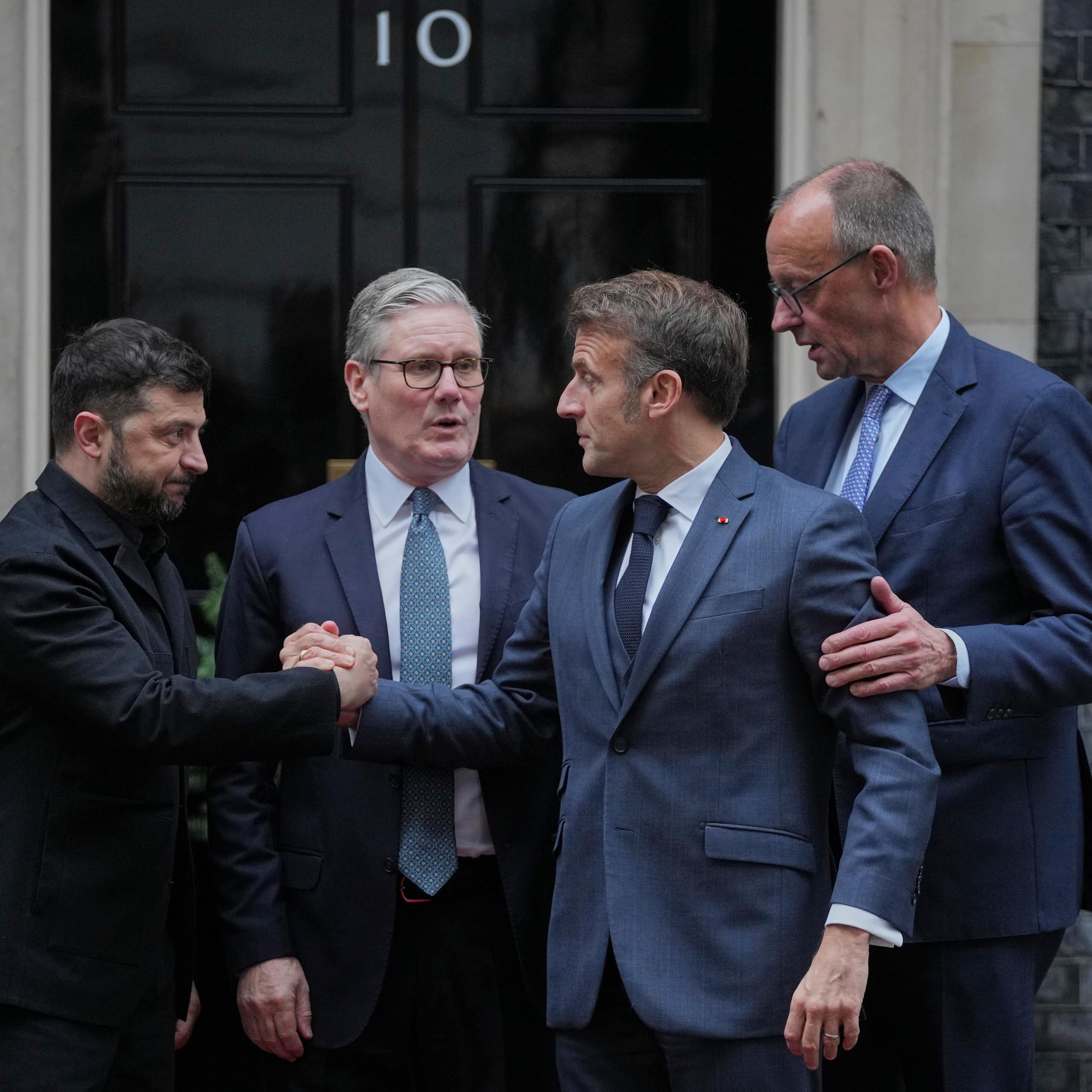 Four men in blue and black suits shake hands as they cluster outside a door with the number 10 on it.
