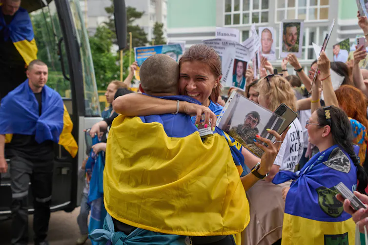 A woman looking very happy embraces a man draped in a blue and gold flag amid a crowd of people outside.