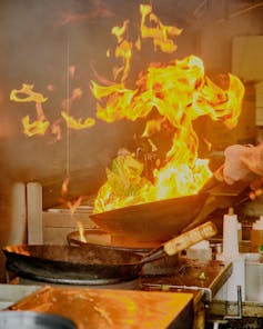 Close-up of flames on a frying pan in a commercial kitchen.