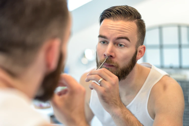 A plan plucking nose hairs in front of a mirror.