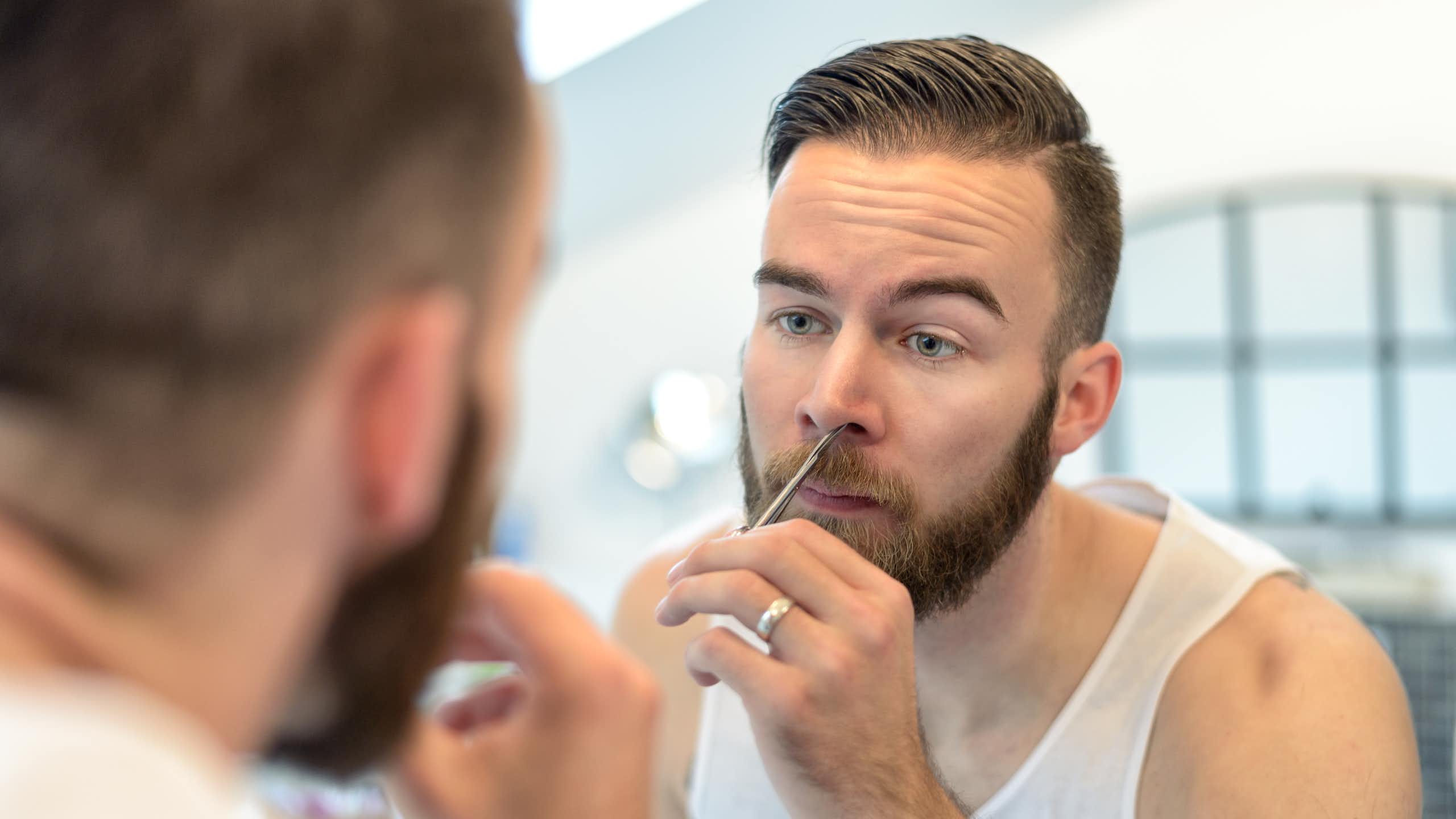 A plan plucking nose hairs in front of a mirror.