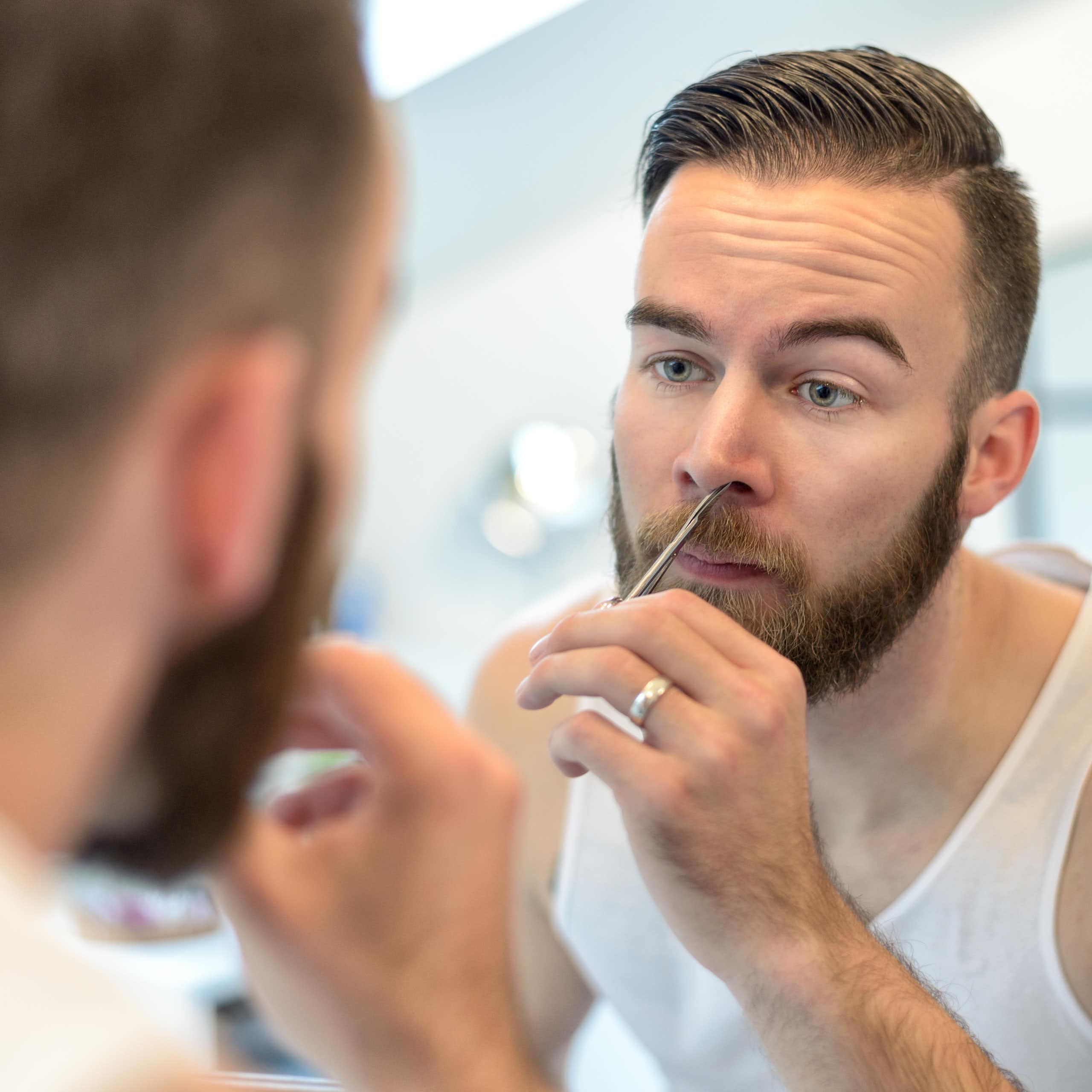 A plan plucking nose hairs in front of a mirror.