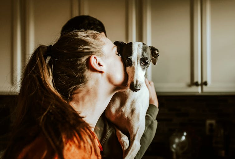 Woman kissing pet dog, burying head in dog's neck
