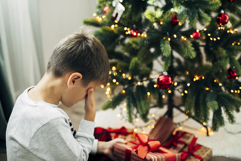 A young child cries in front of a Christmas tree.