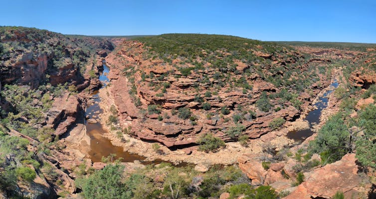 Panoramic view of a river valley with characteristic outback red rocks and green foliage.
