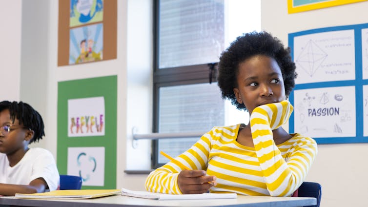 A girl sitting in class with her head resting on her hand, looking away from her desk dreamily.