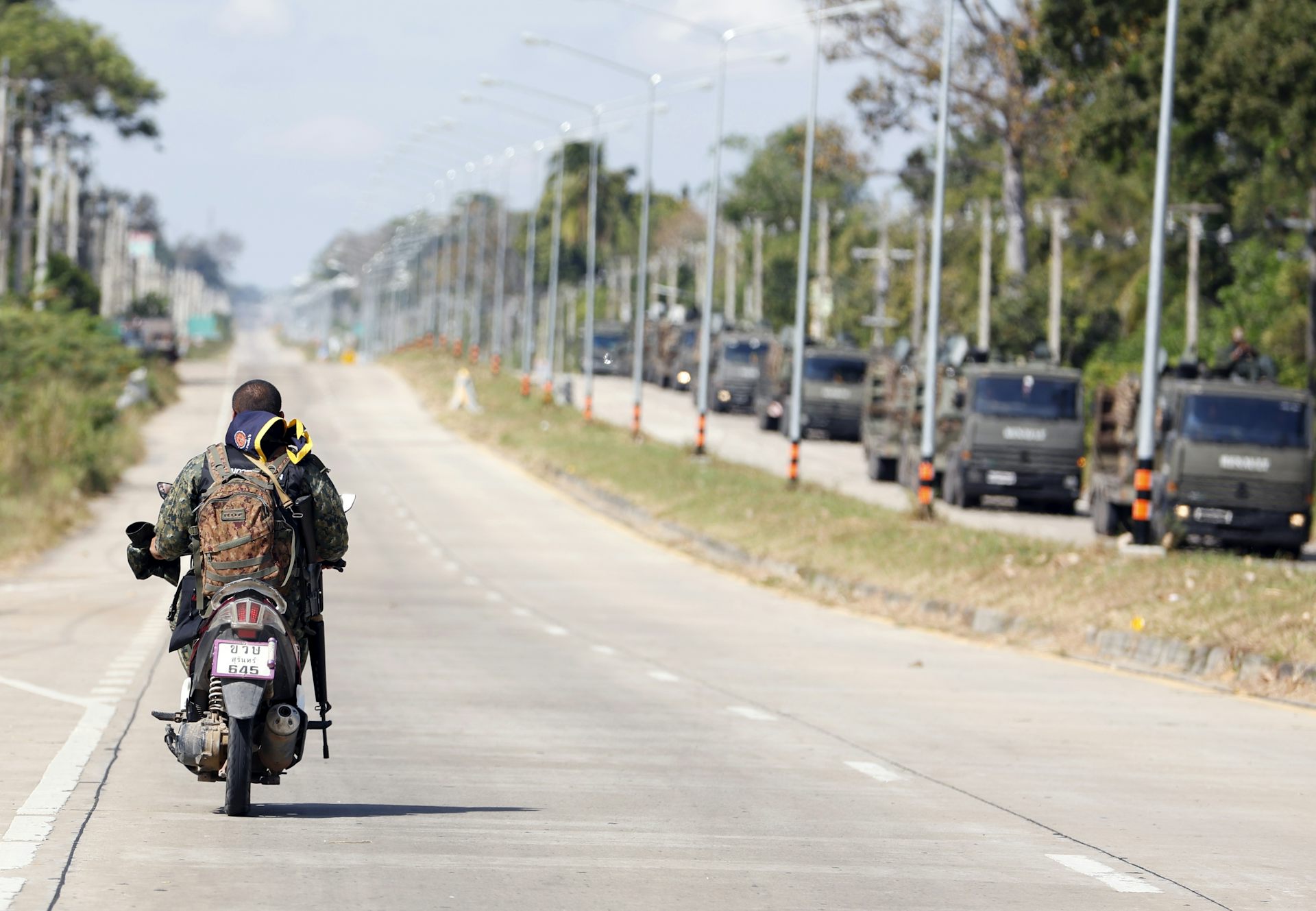 An armed Thai soldier patrols on a motorbike alongside a convoy of armoured military vehicles.
