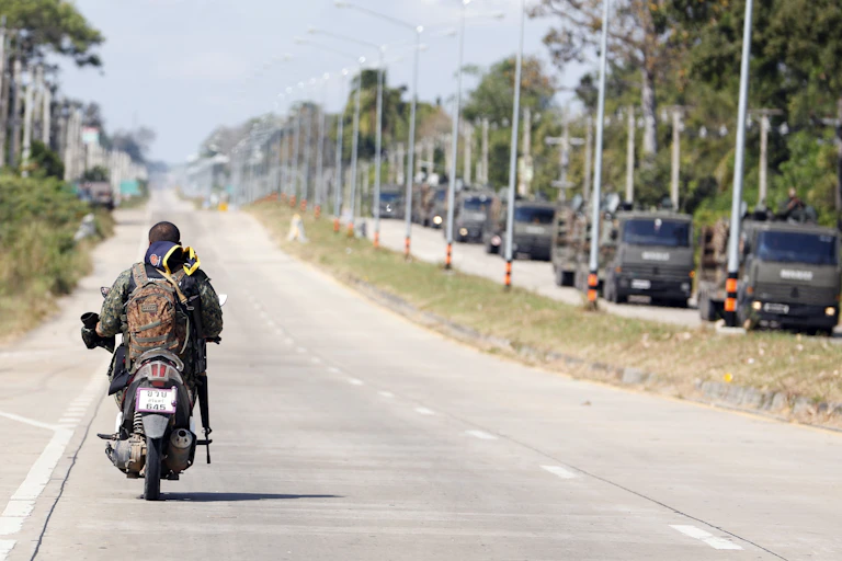 An armed Thai soldier patrols on a motorbike alongside a convoy of armoured military vehicles.