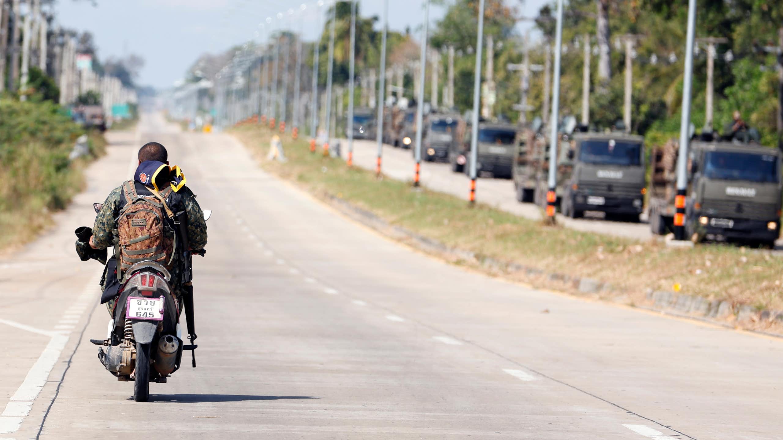 An armed Thai soldier patrols on a motorbike alongside a convoy of armoured military vehicles.