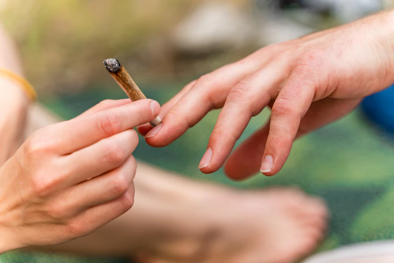 One hand passes a cannabis cigarette to another hand.