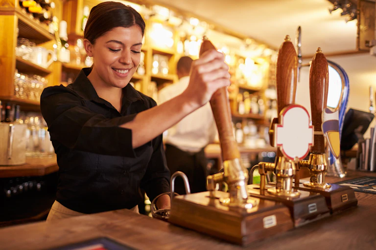 young woman behind a bar pulling a pint.