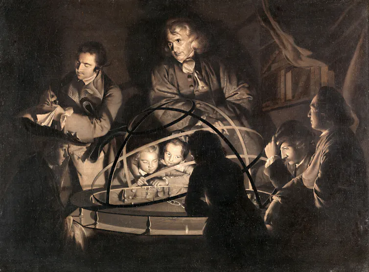 People in 1700s garb listen as a philosopher describes the orrery they're gathered around