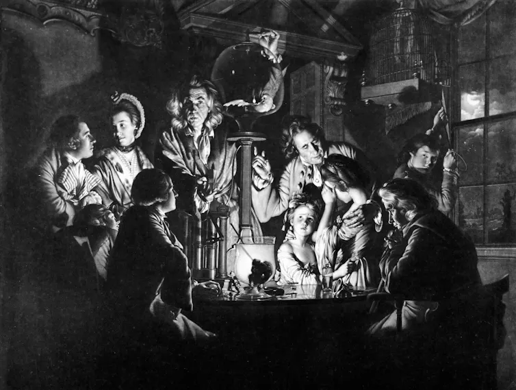people in 1700s clothes gather around a column with a glass globe on top with one man talking and gesturing