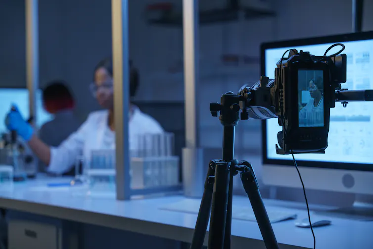 camera captures woman in white coat holding glassware in lab