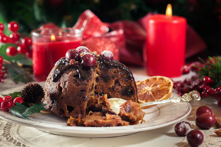 Partially eaten Christmas pudding with red festive decorations in background