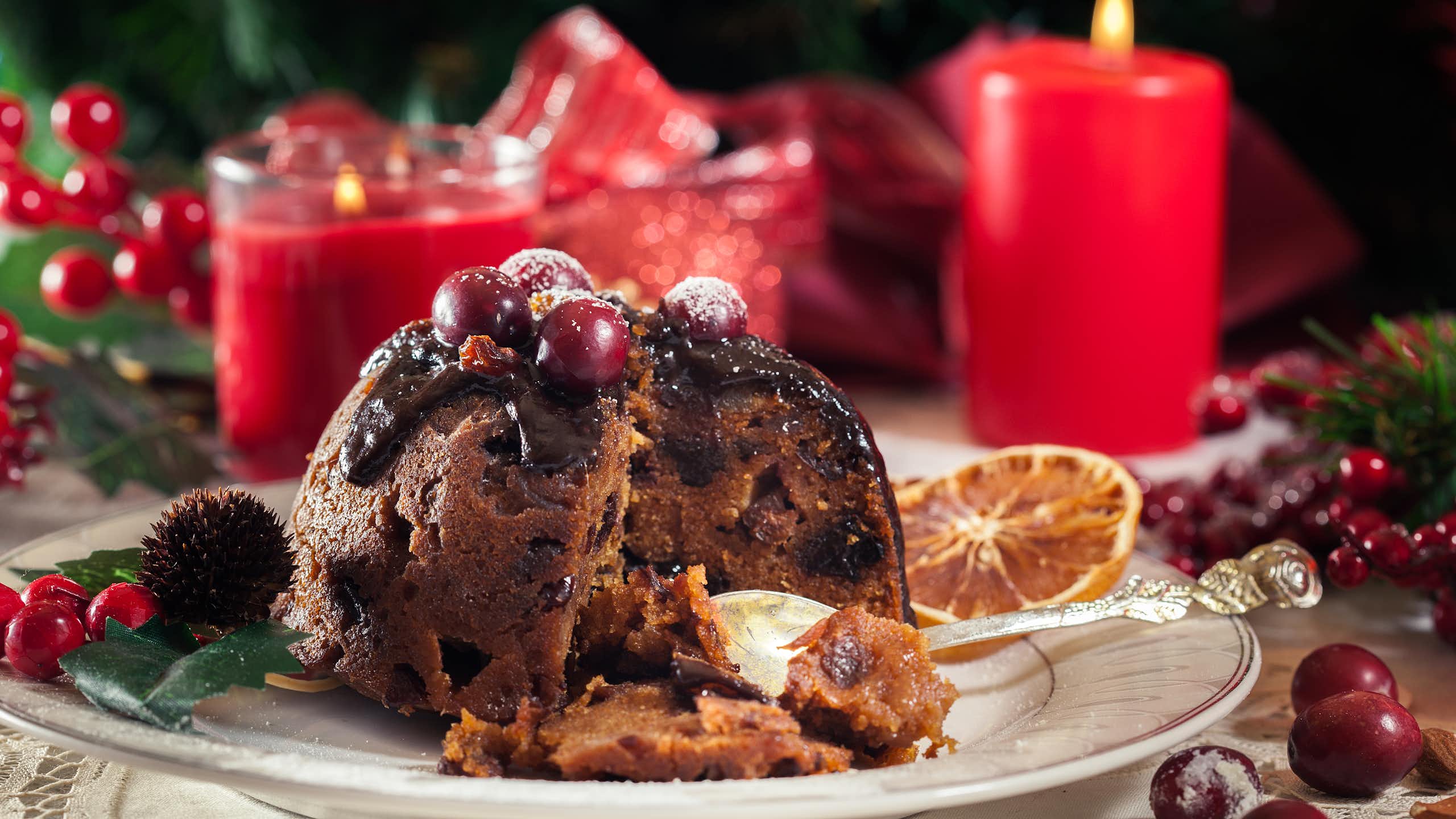 Partially eaten Christmas pudding with red festive decorations in background