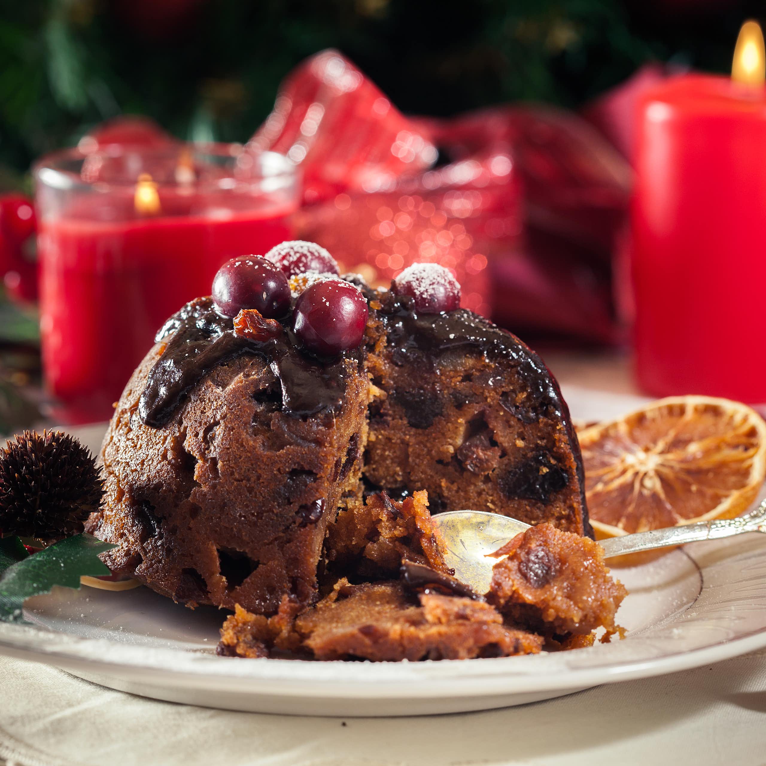 Partially eaten Christmas pudding with red festive decorations in background