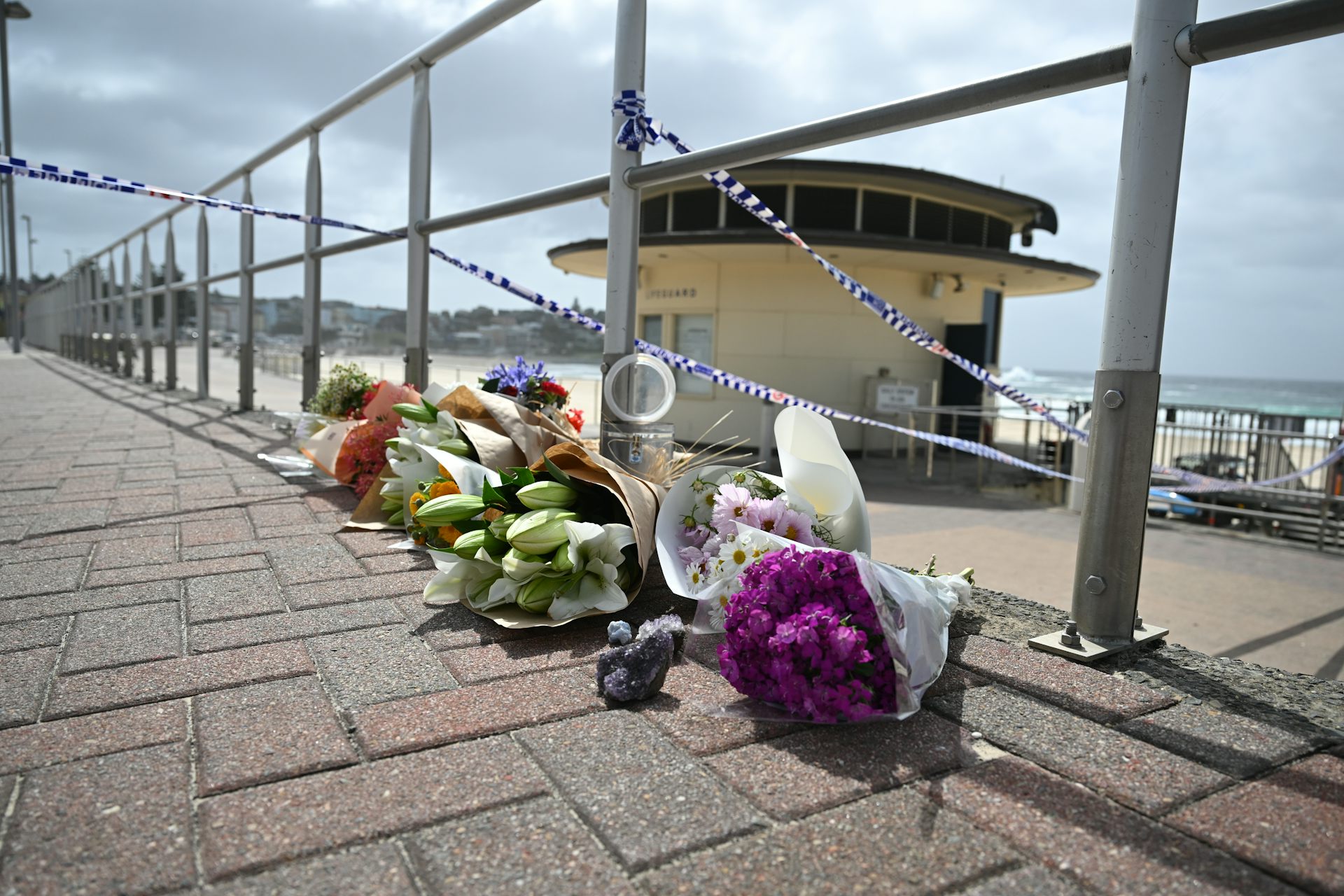 Bouquets of flowers under police tape at Bondi beach.
