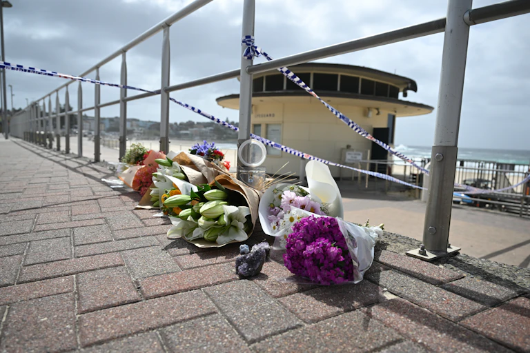 Bouquets of flowers under police tape at Bondi beach.