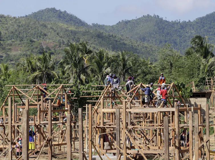 Building workers stand on the roof of a timber house frame.