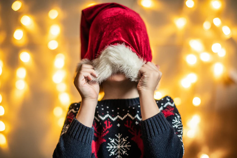 A young child pulls a Santa hat down over their eyes