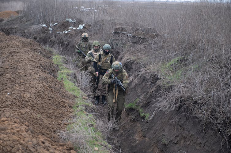 A group of four Russian servicemen walk along a trench in Ukraine.