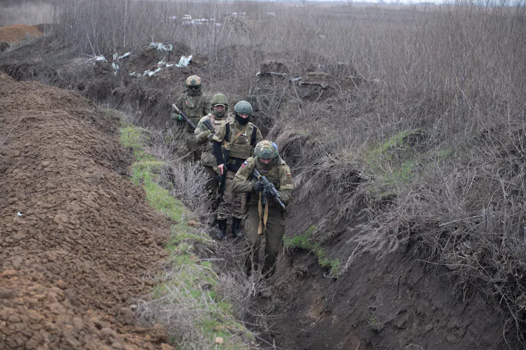 A group of four Russian servicemen walk along a trench in Ukraine.