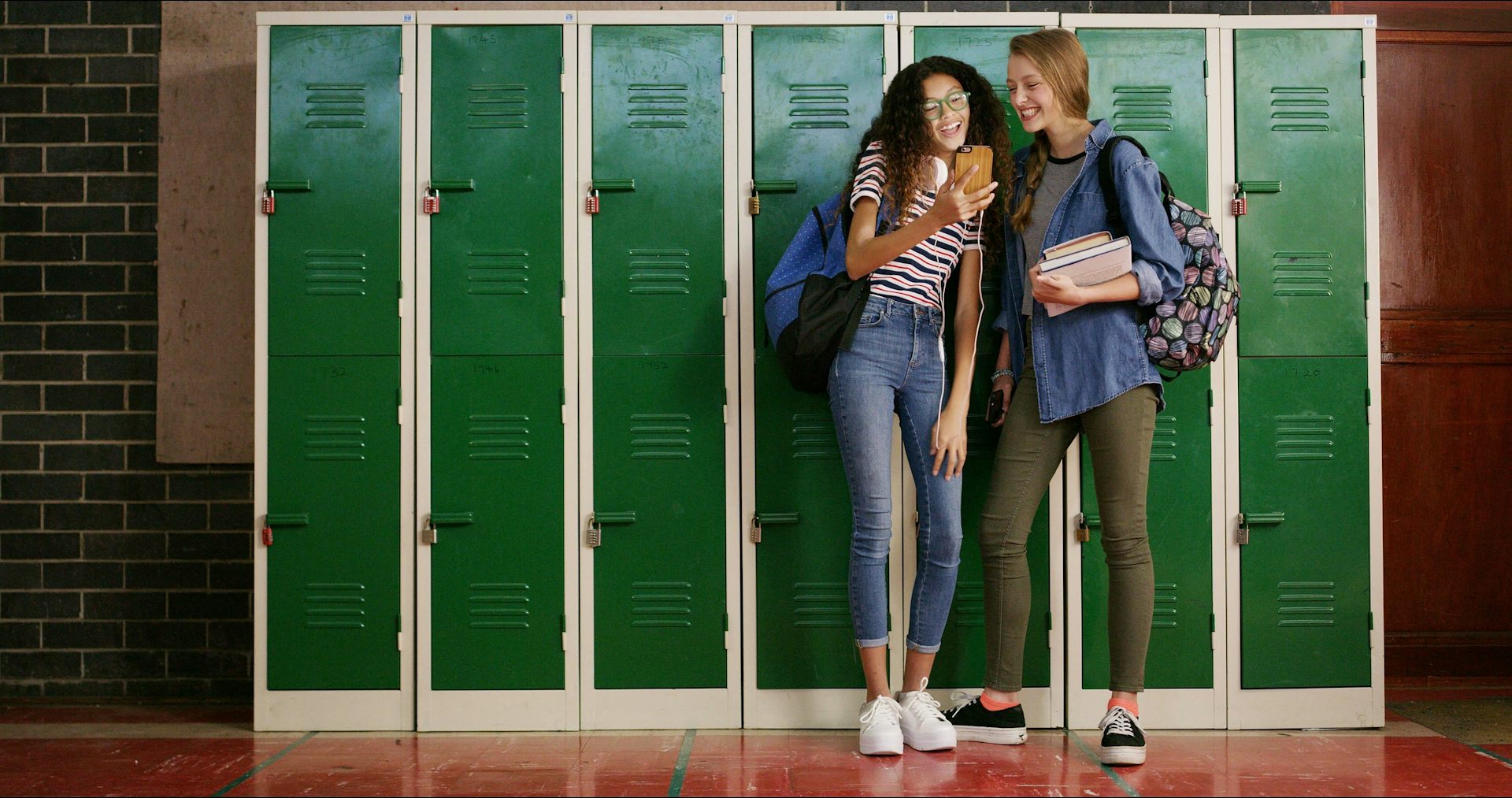 Two girls in a school laughing at a phone
