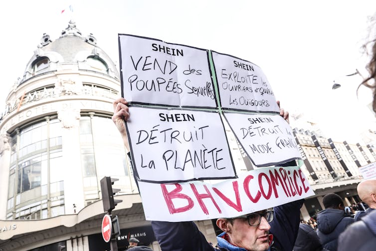 male protester holding up sign outside paris department store that houses a shein concession.