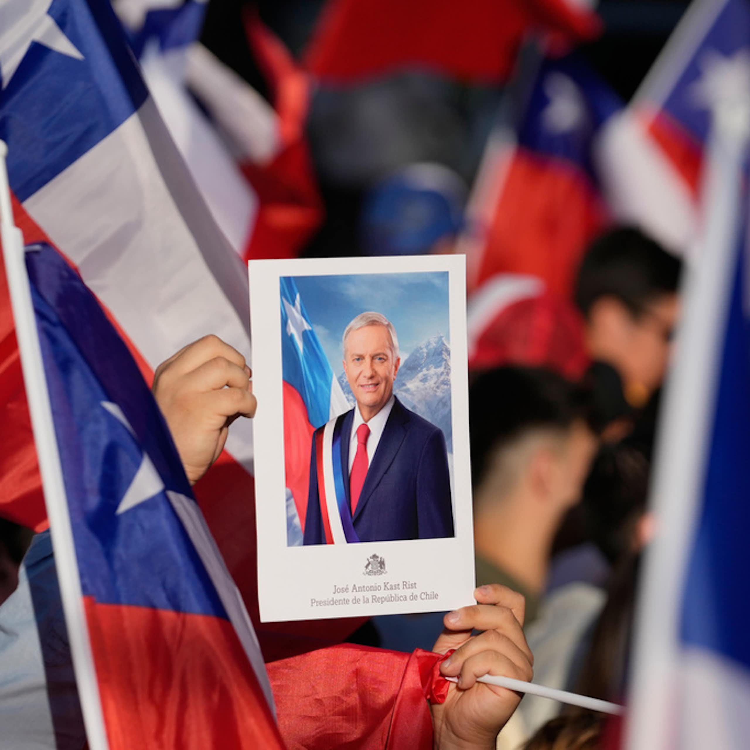 People hold flags and a picture of their leader at a political rally.