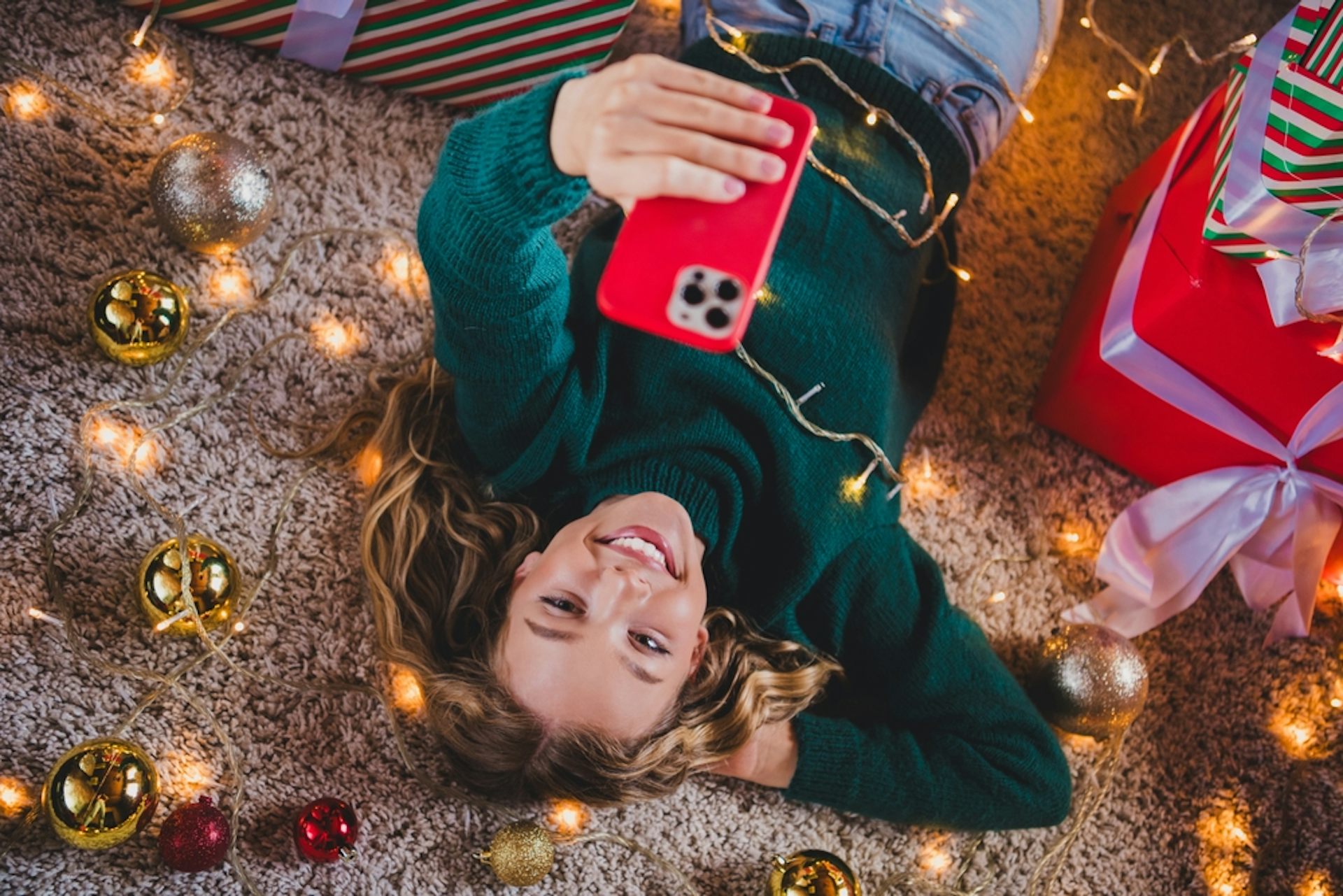 Teen girl lying on the floor looking at her phone surrounded by Christmas things