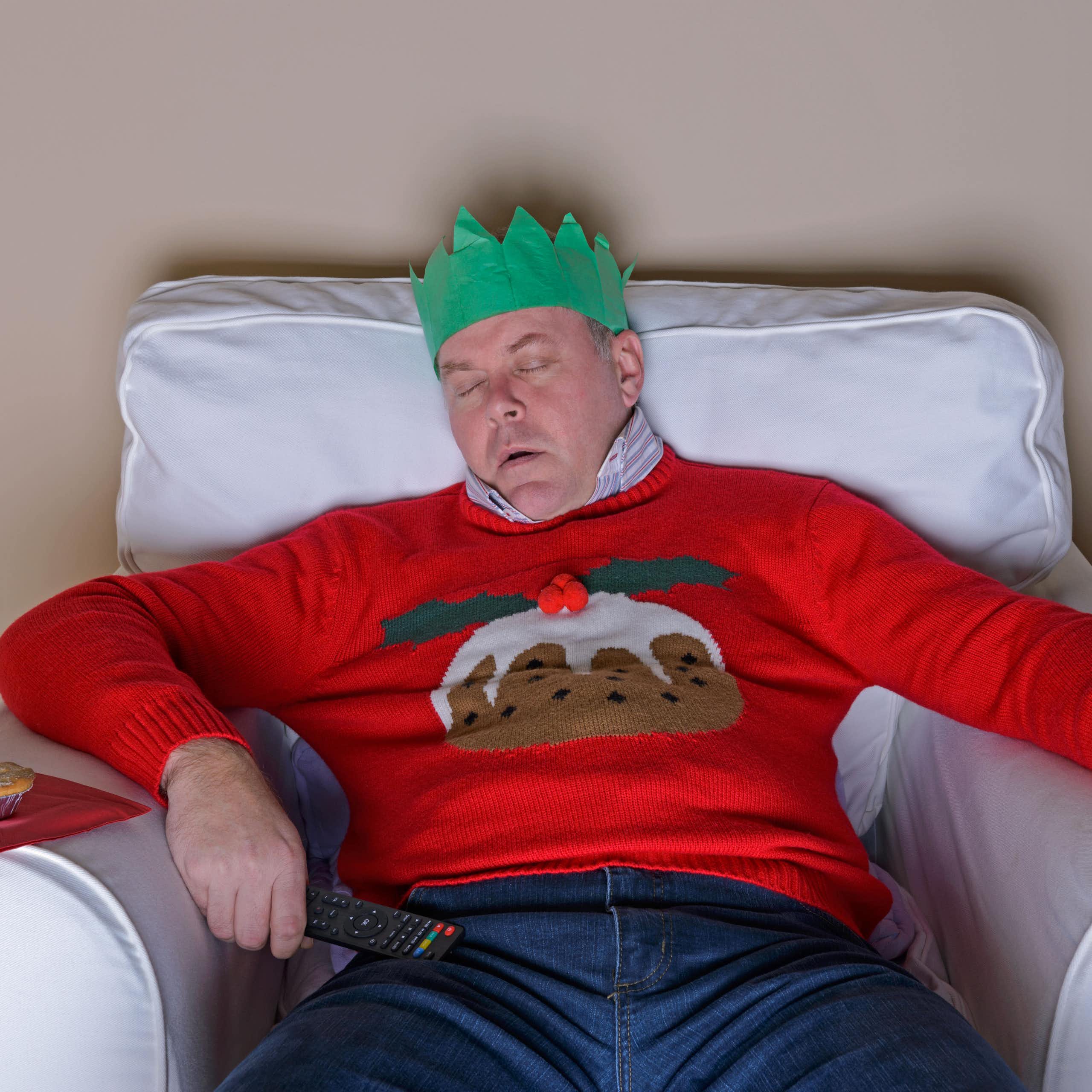 Middle-aged man sleeping with a Christmas hat on, glass of cognac in his hand.