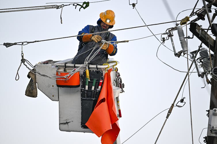 A person in an elevated bucket works with tools and wires.