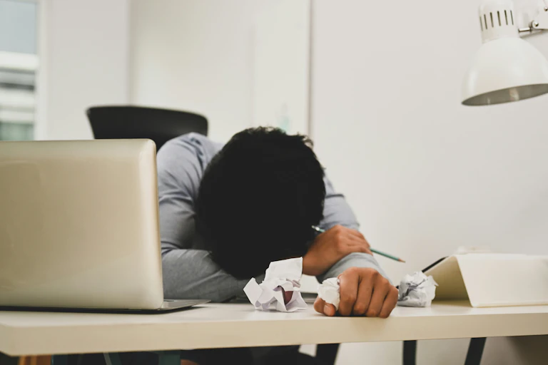 Une personne posant sa tête sur ses bras alors qu'elle est assise à un bureau.