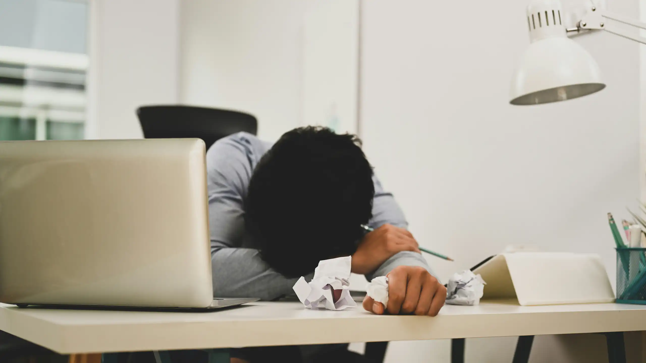 Une personne posant sa tête sur ses bras alors qu'elle est assise à un bureau.