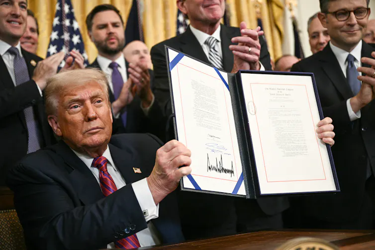 A man in a suit holds up a folder with writing on it.