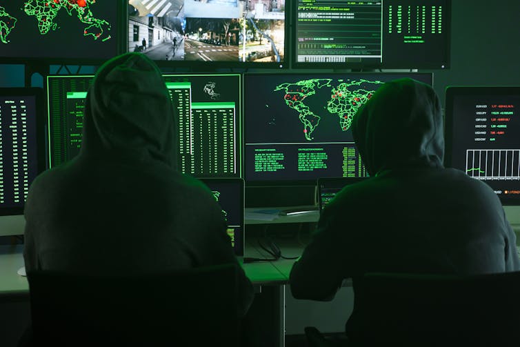 Two men in hoods sit in front of computer screens.