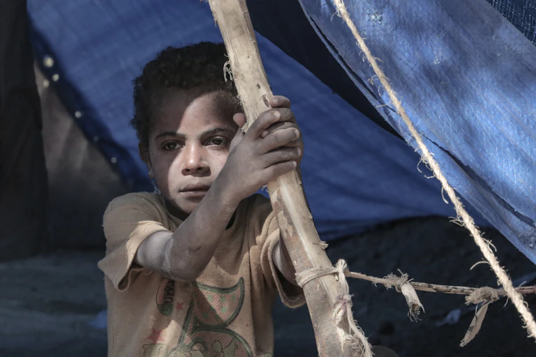 A child stares out from a tent as a refugee camp