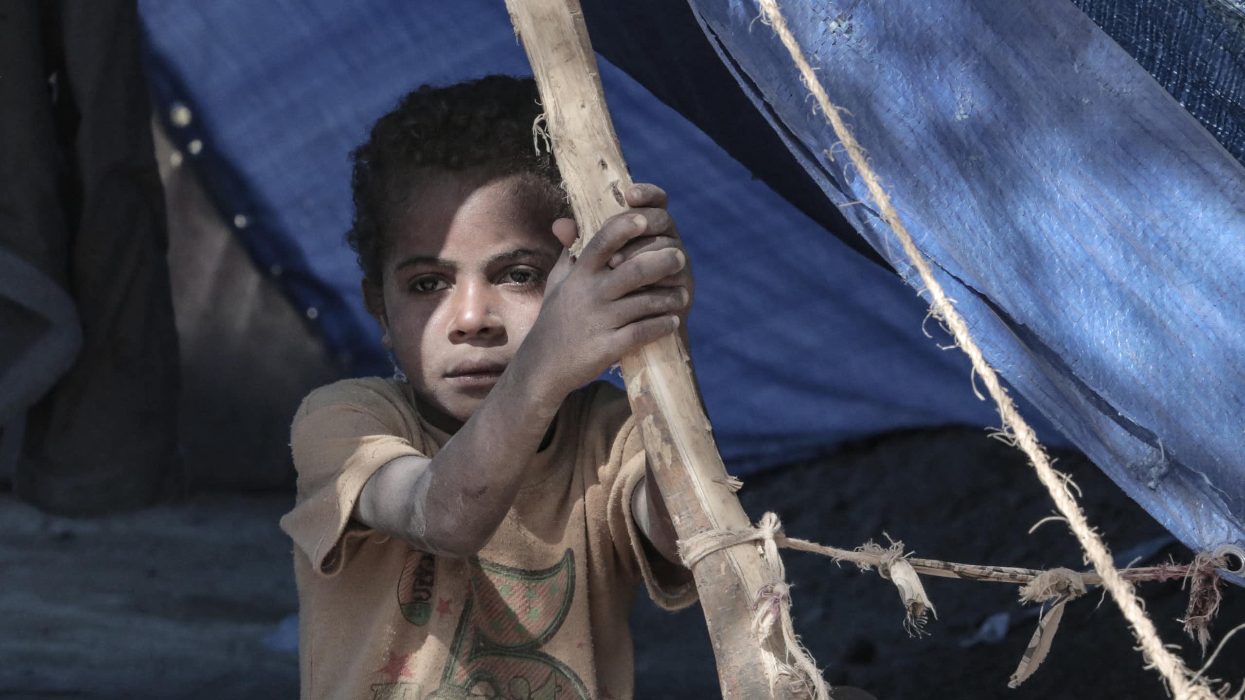 A child stares out from a tent as a refugee camp