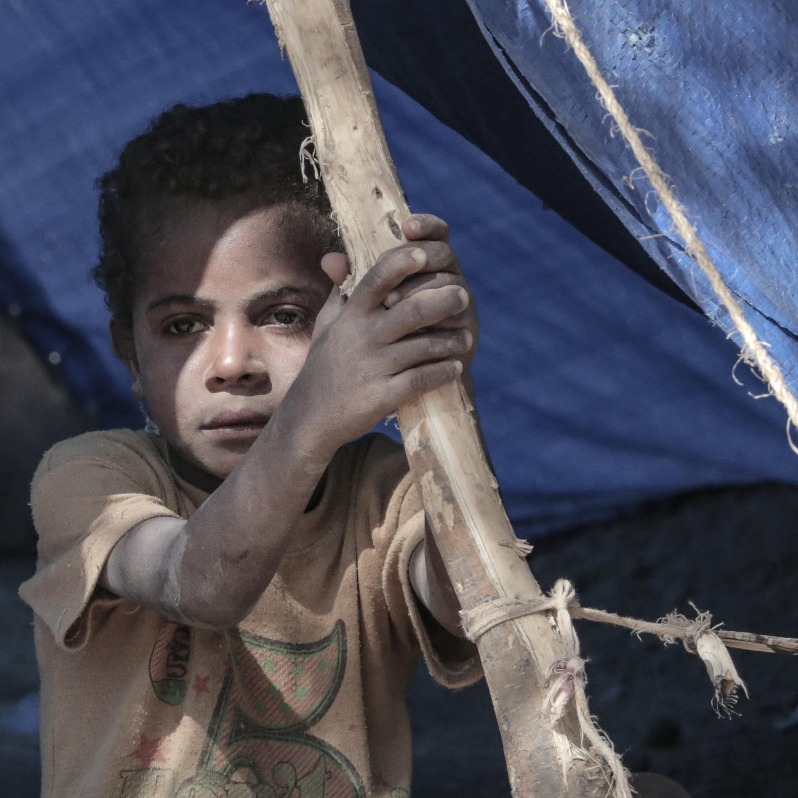 A child stares out from a tent as a refugee camp