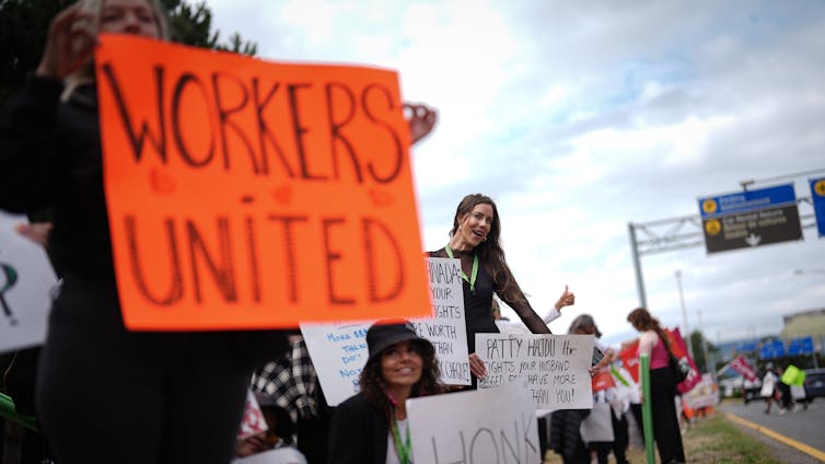 Los trabajadores en huelga esperan señales. El cartel naranja en primer plano dice Trabajadores Unidos.