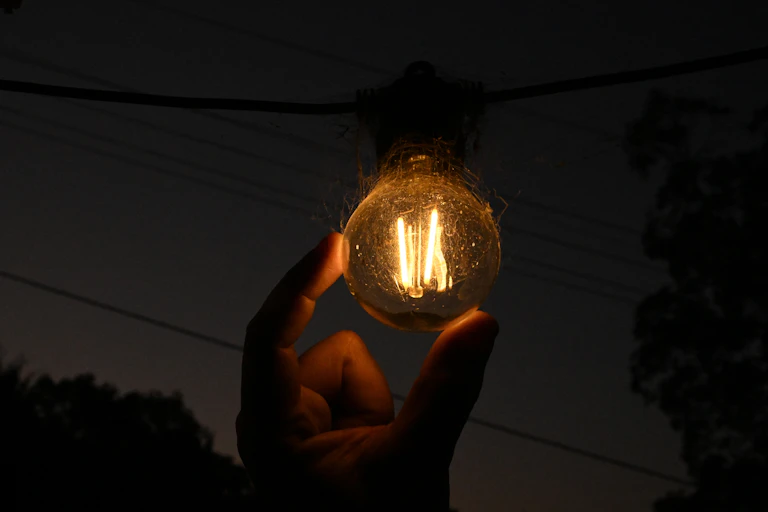 lightbulb held in hand against dark sky