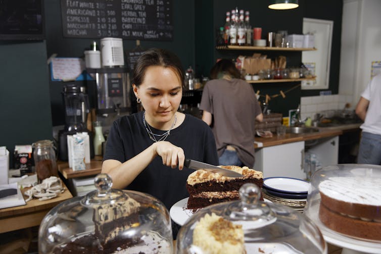 A teenage girl cuts a slice of cake in a cafe