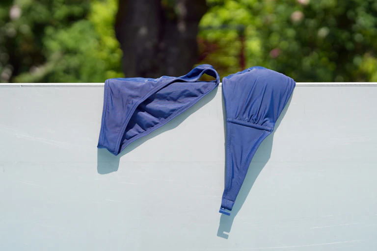 A navy bikini drying draped over a fence.